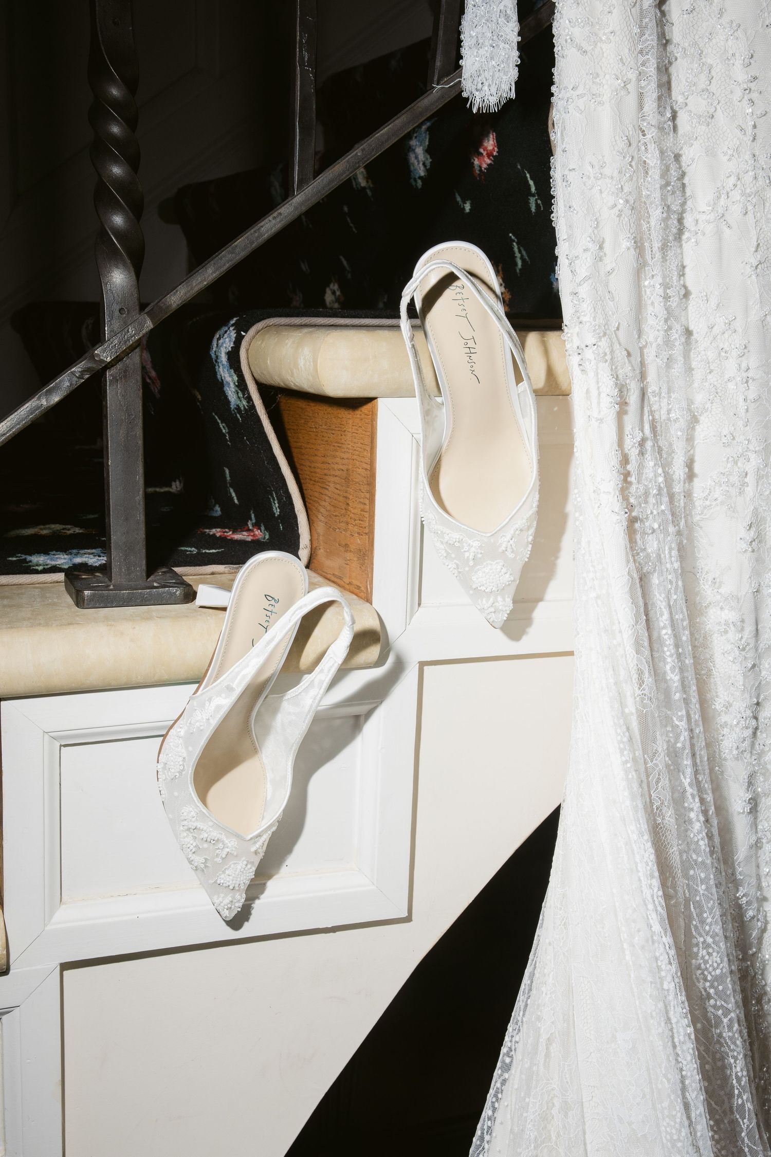 White high heel shoes displayed on a shelf against a dark background with sheer white curtains.