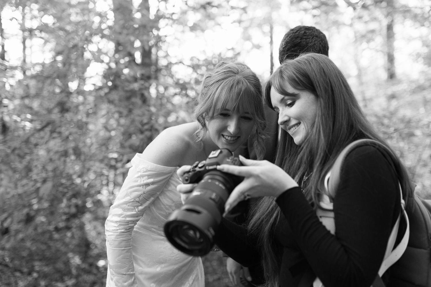Two photographers in casual attire review images on a camera's display screen in a black and white photo.