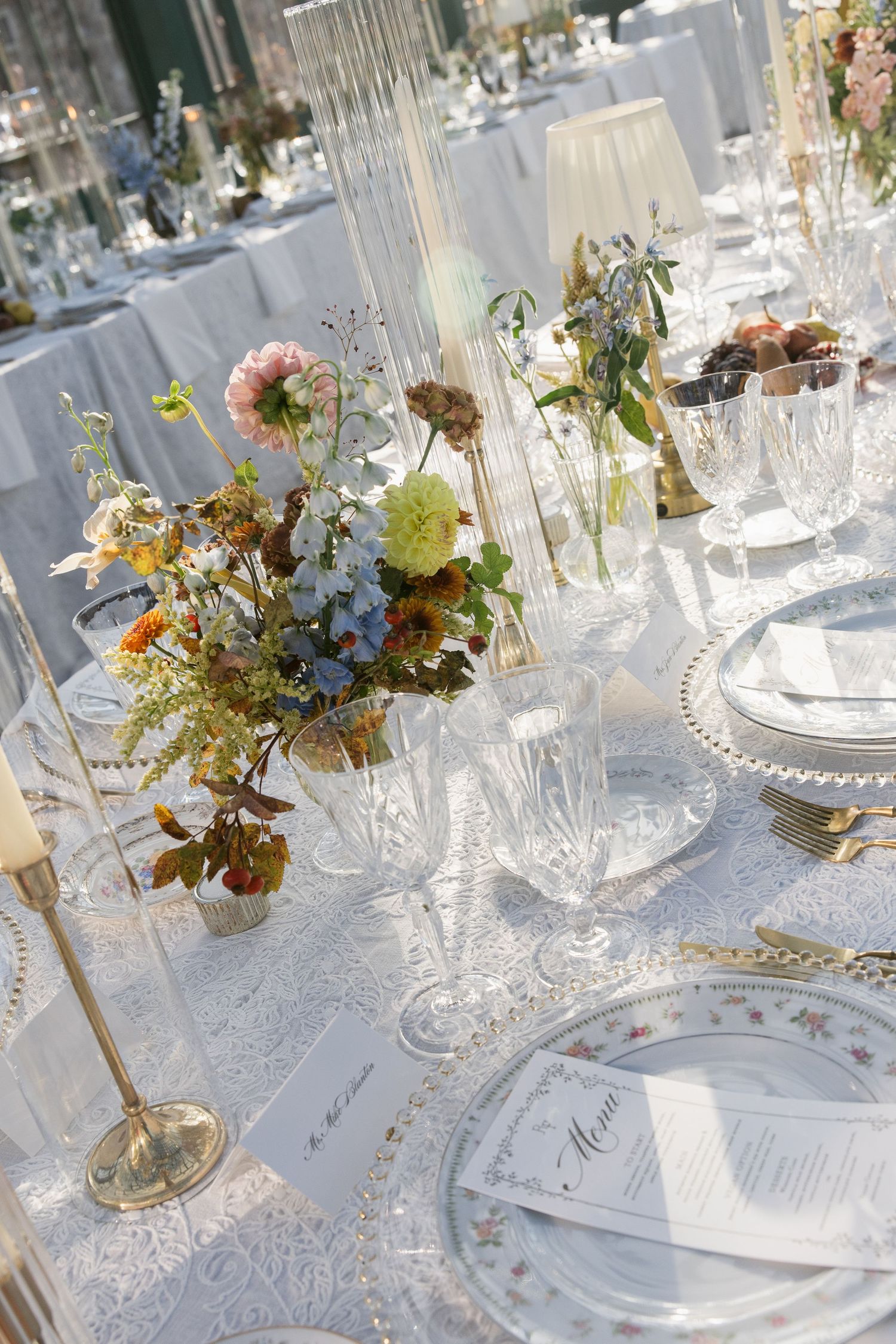 Elegant wedding table settings with crystal glassware and delicate floral centerpieces in soft pastel colors.