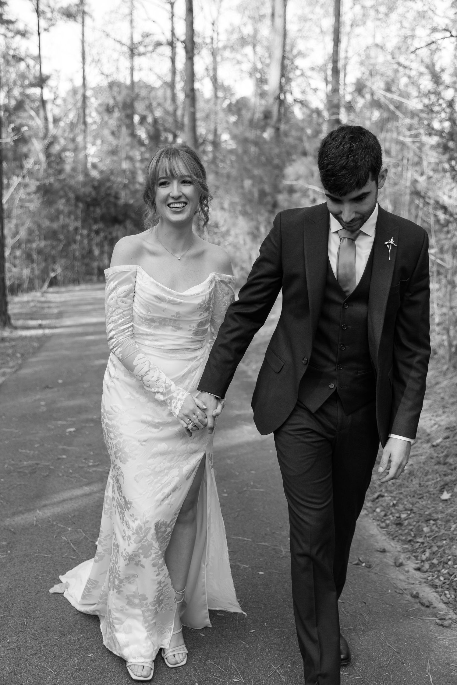 Black and white wedding photos show a couple walking and laughing together on a tree-lined path in casual candid moments.