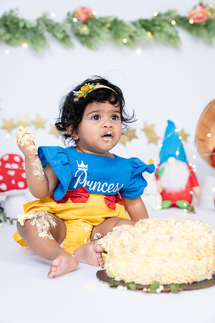 A delightful cake smash captures the celebration of a first birthday, featuring a snow white theme backdrop and an adora