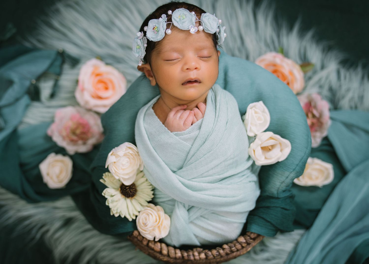 a newborn baby girl sleeping in a basket set against flowers and greenery