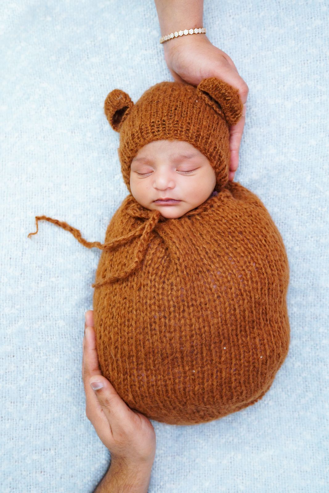 Newborn baby swaddled in a knitted cocoon, parents tenderly pose for a fine art newborn photo