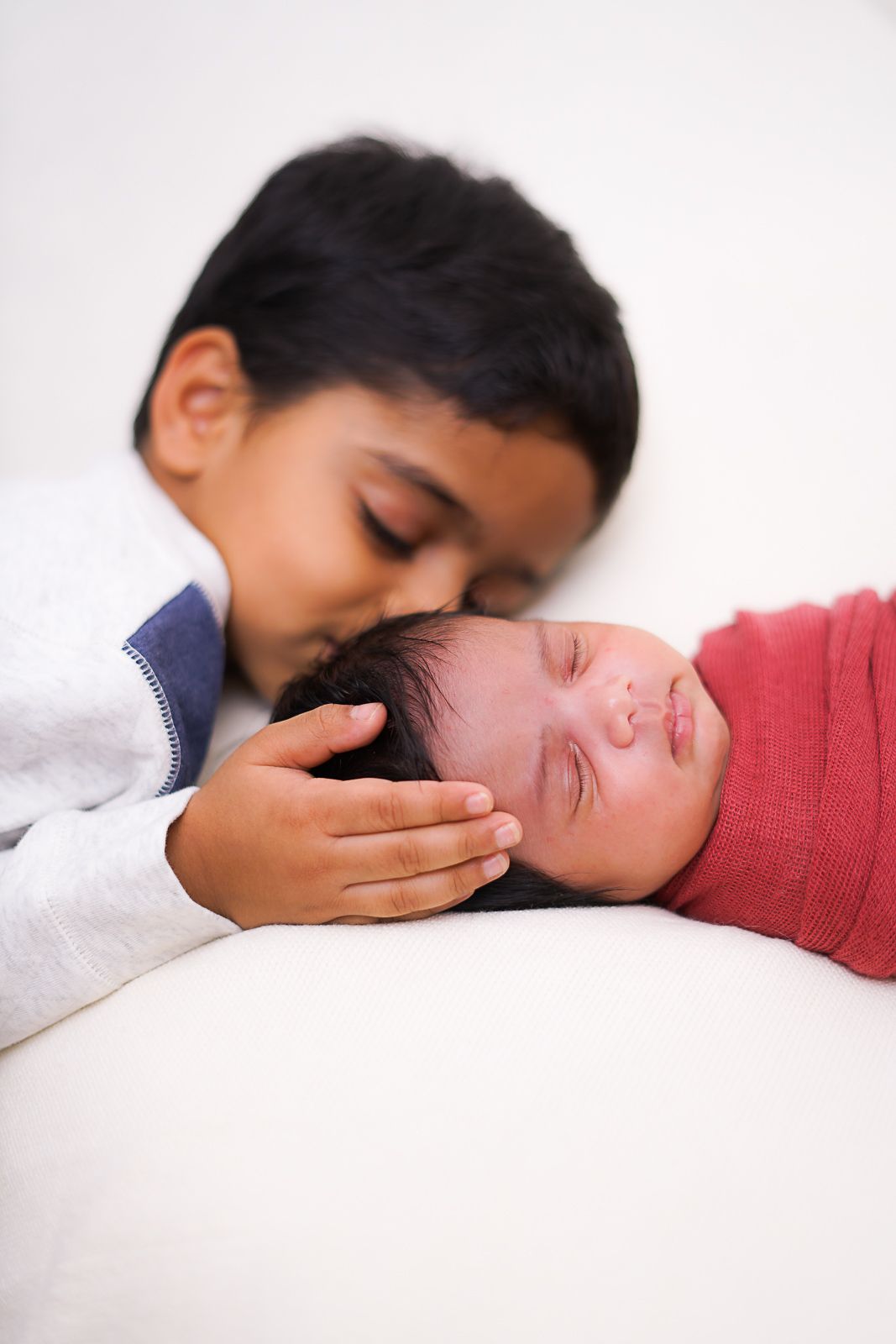 Brother tenderly kisses his newborn sister in a heartwarming sibling moment captured during a newborn photoshoot