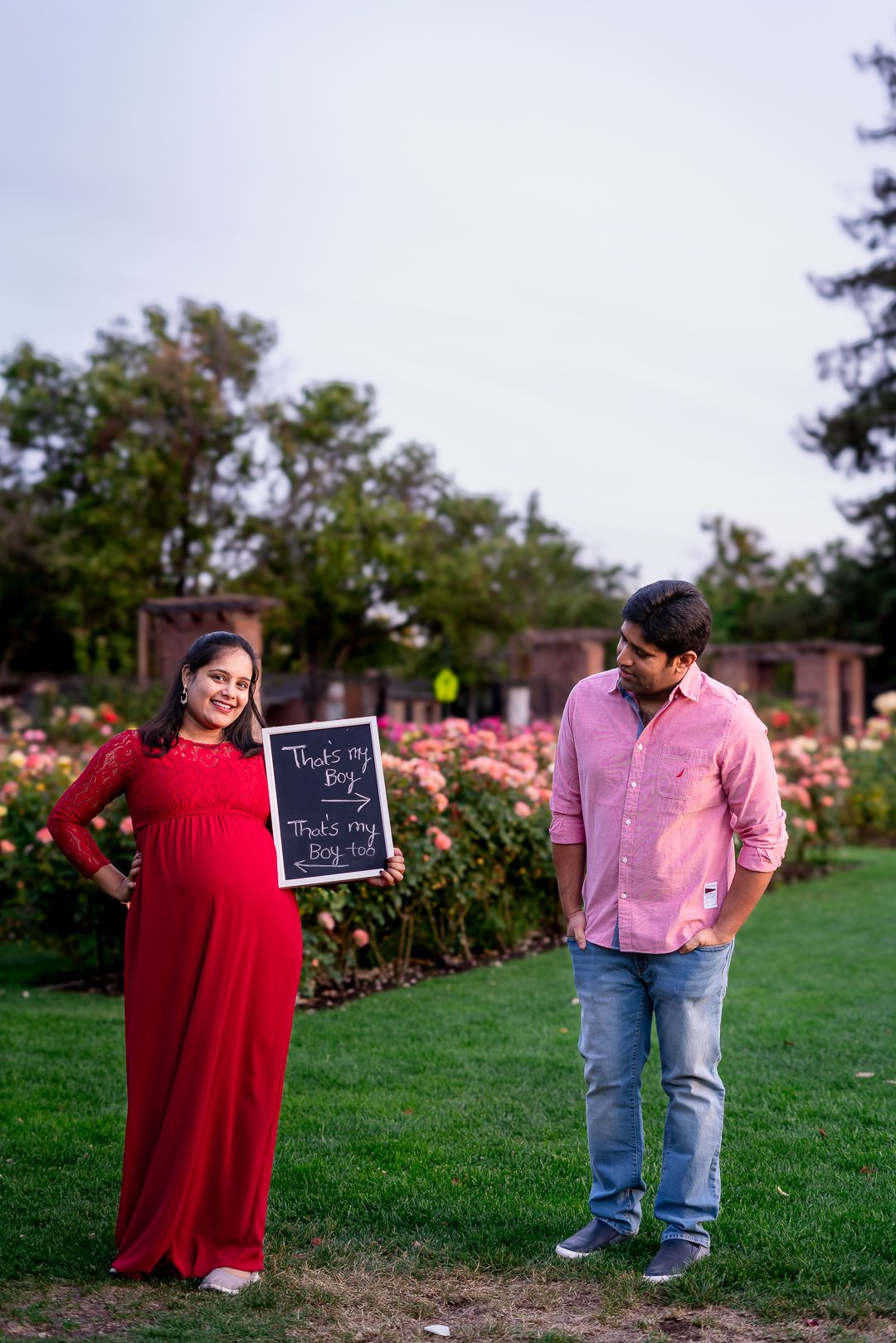 Pose idea for Expecting parents with a fun chalkboard message announcing baby boy arrival by rose bushes in San Jose