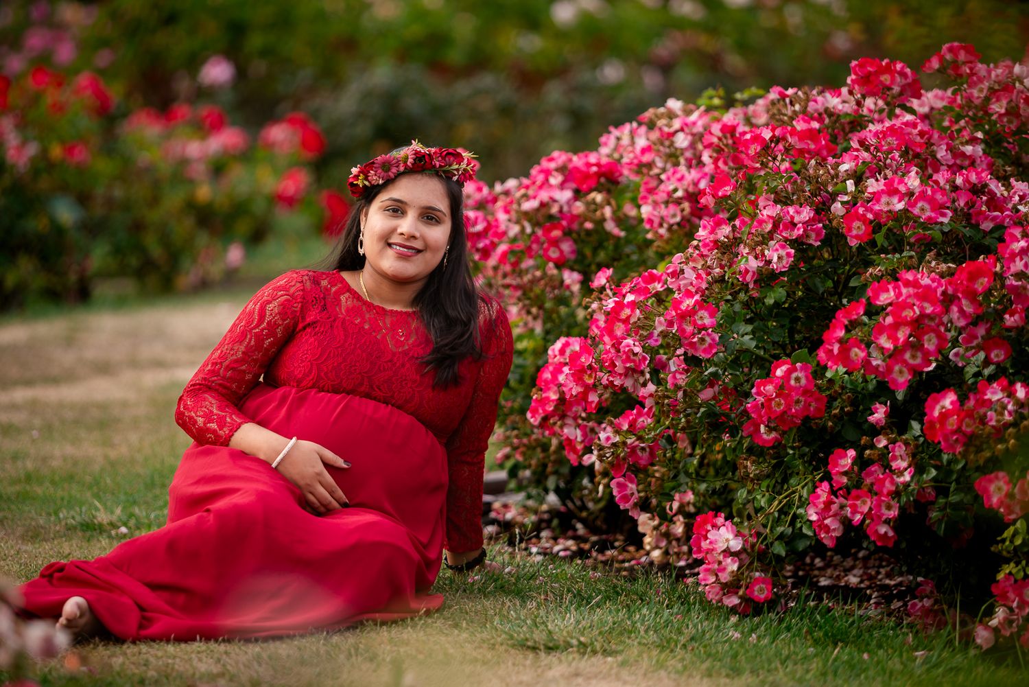 Pose idea of Expecting mother sitting against therose arches in Bay Area garden portrait session glowing in her bump