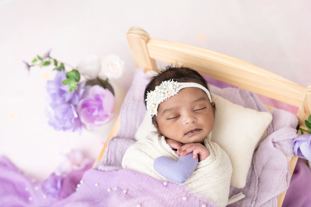 Newborn baby girl swaddled in lavender wrap lying peacefully on a baby bed during Tracy, CA newborn session