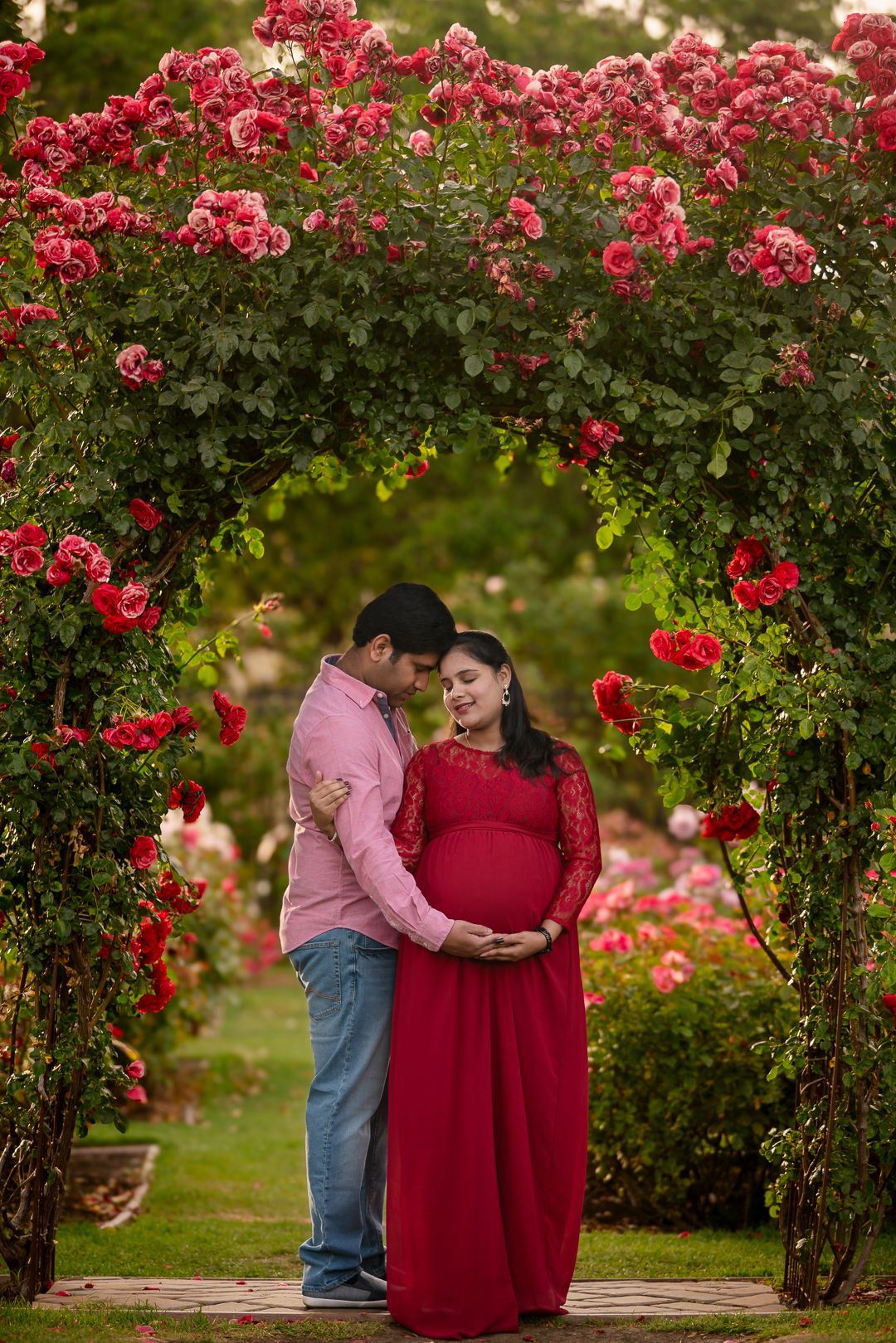 Colorful spring maternity photo near San Jose Rose Garden rose Arch couple leaning into each other holding bump