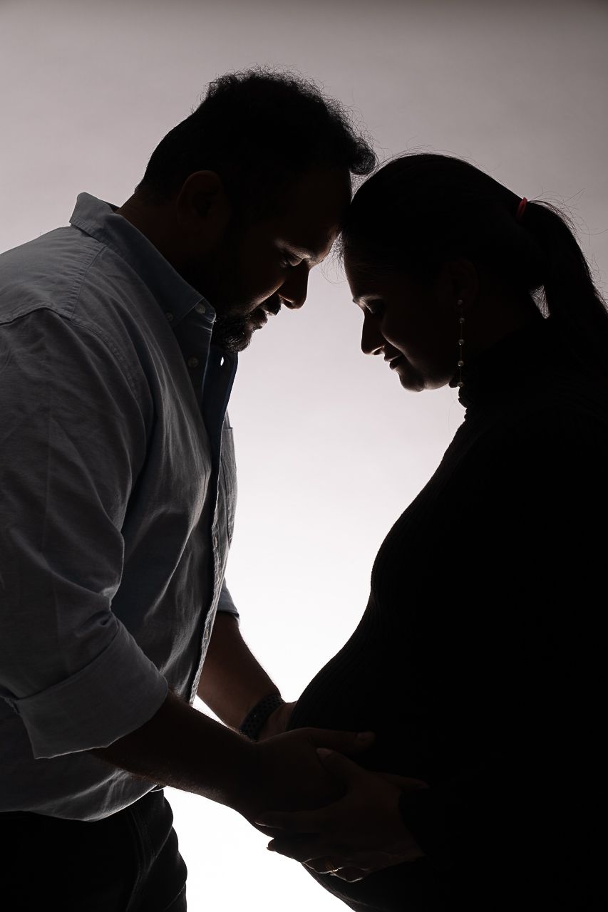 Silhouette of pregnant couple touching foreheads embracing the family bond in a studio photo session in tracy, CA