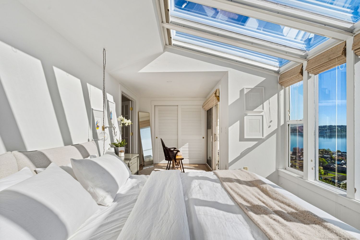 Bright white bedroom with skylights, large windows overlooking water, hardwood floors, and abundant natural light.