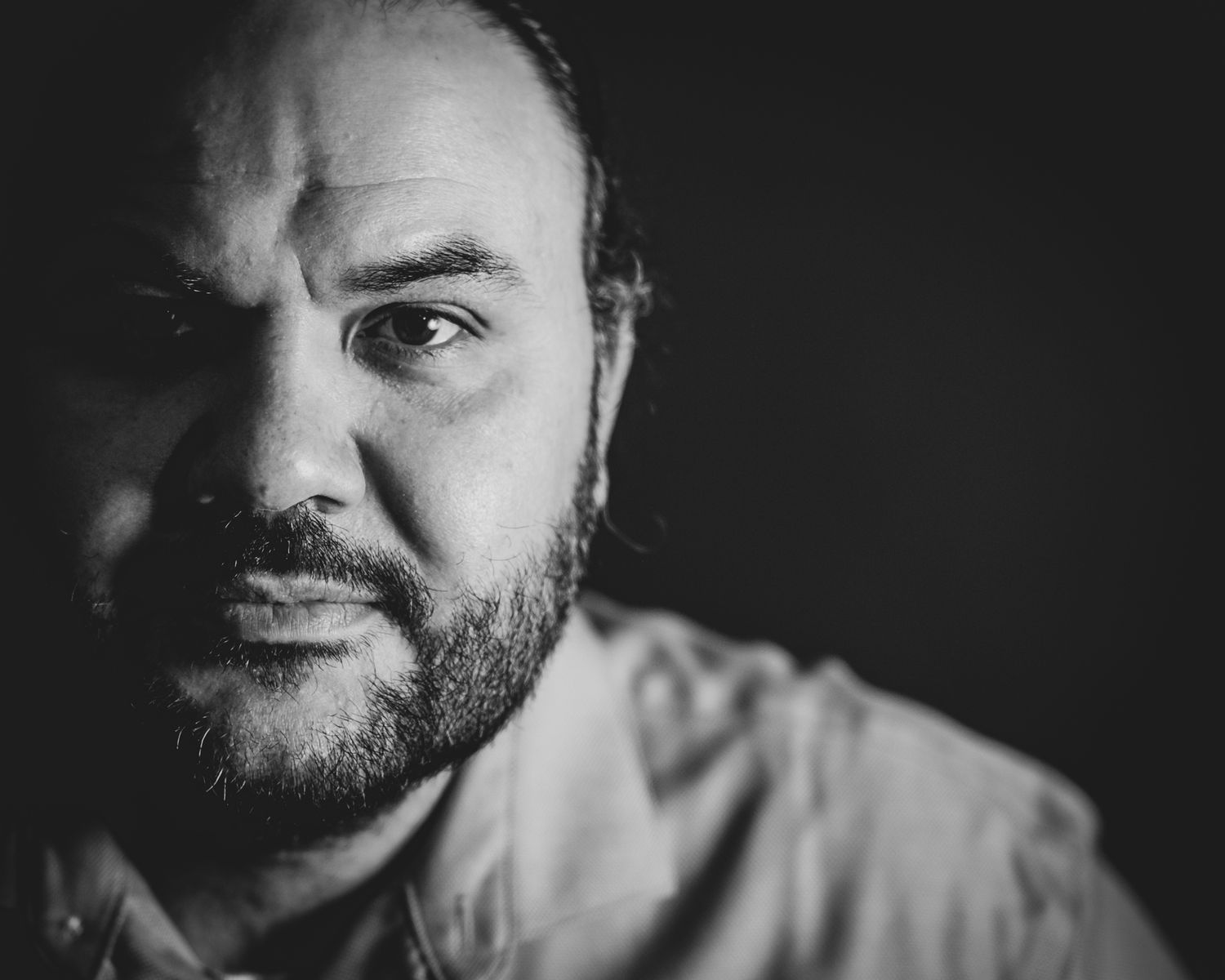 A dramatic black and white portrait showing a serious expression with soft lighting against a dark background.