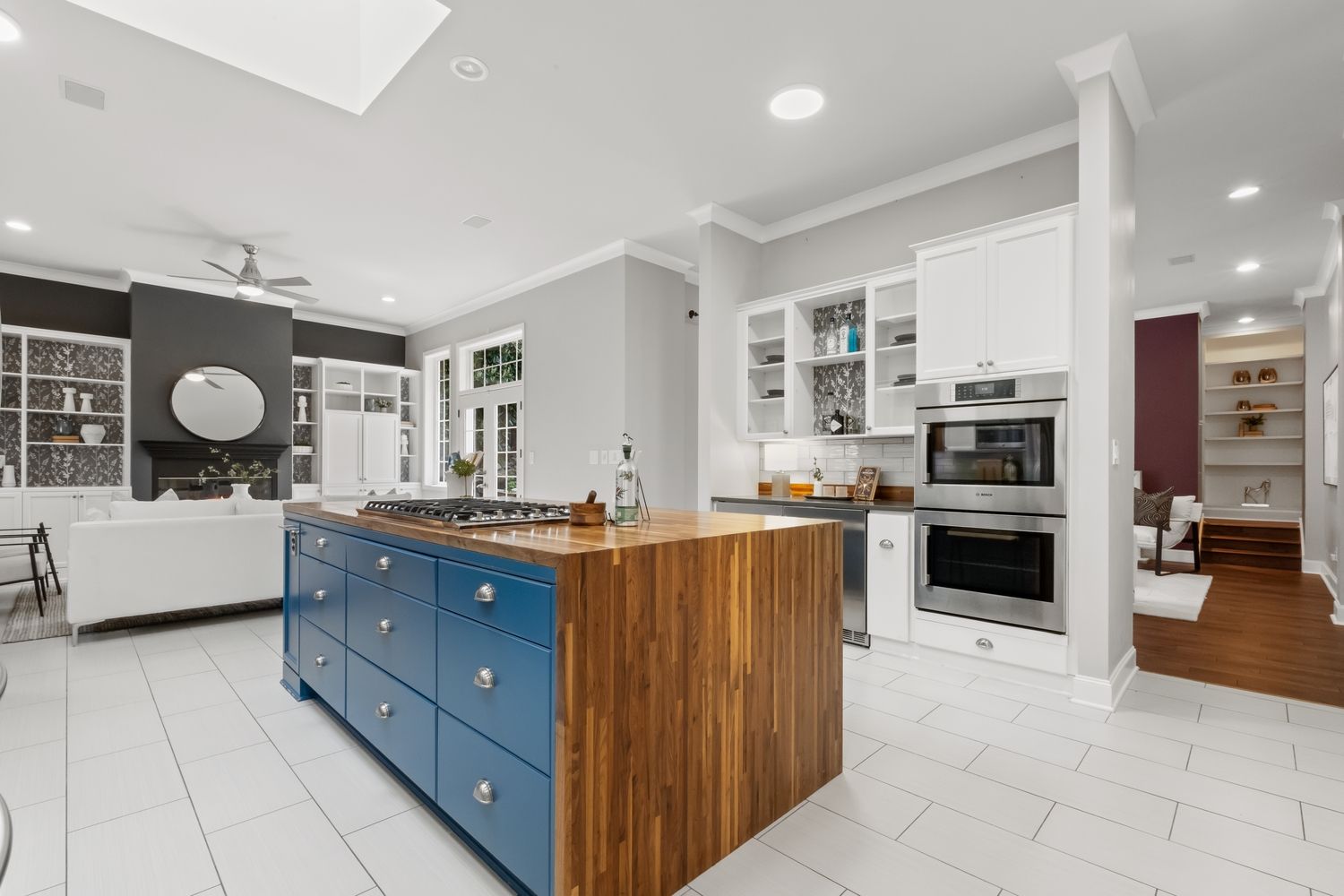 Modern kitchen with blue island, butcher block countertop, white cabinets, stainless appliances, and open living area.