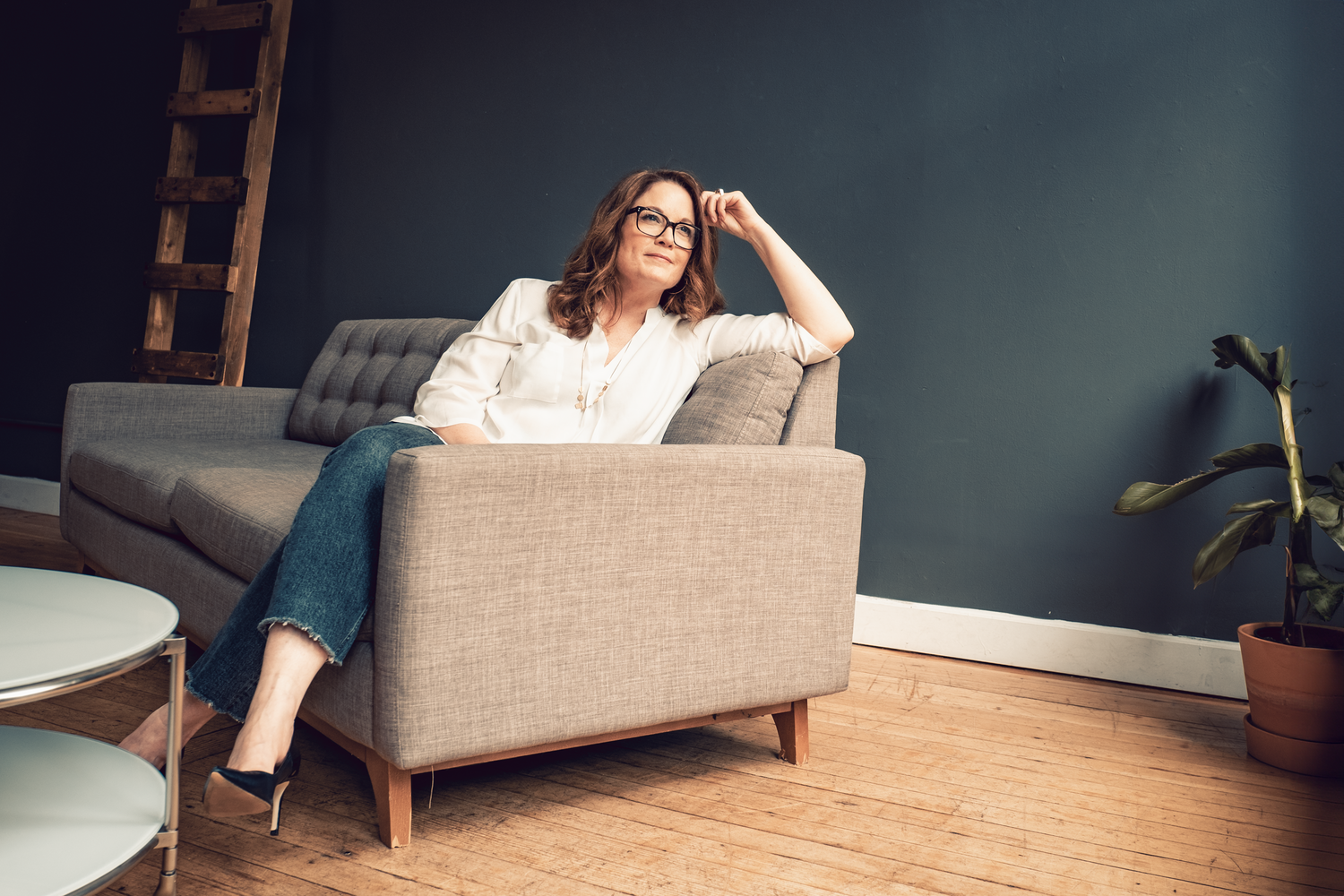 Woman relaxing on modern gray armchair in living room with hardwood floors and navy blue walls.