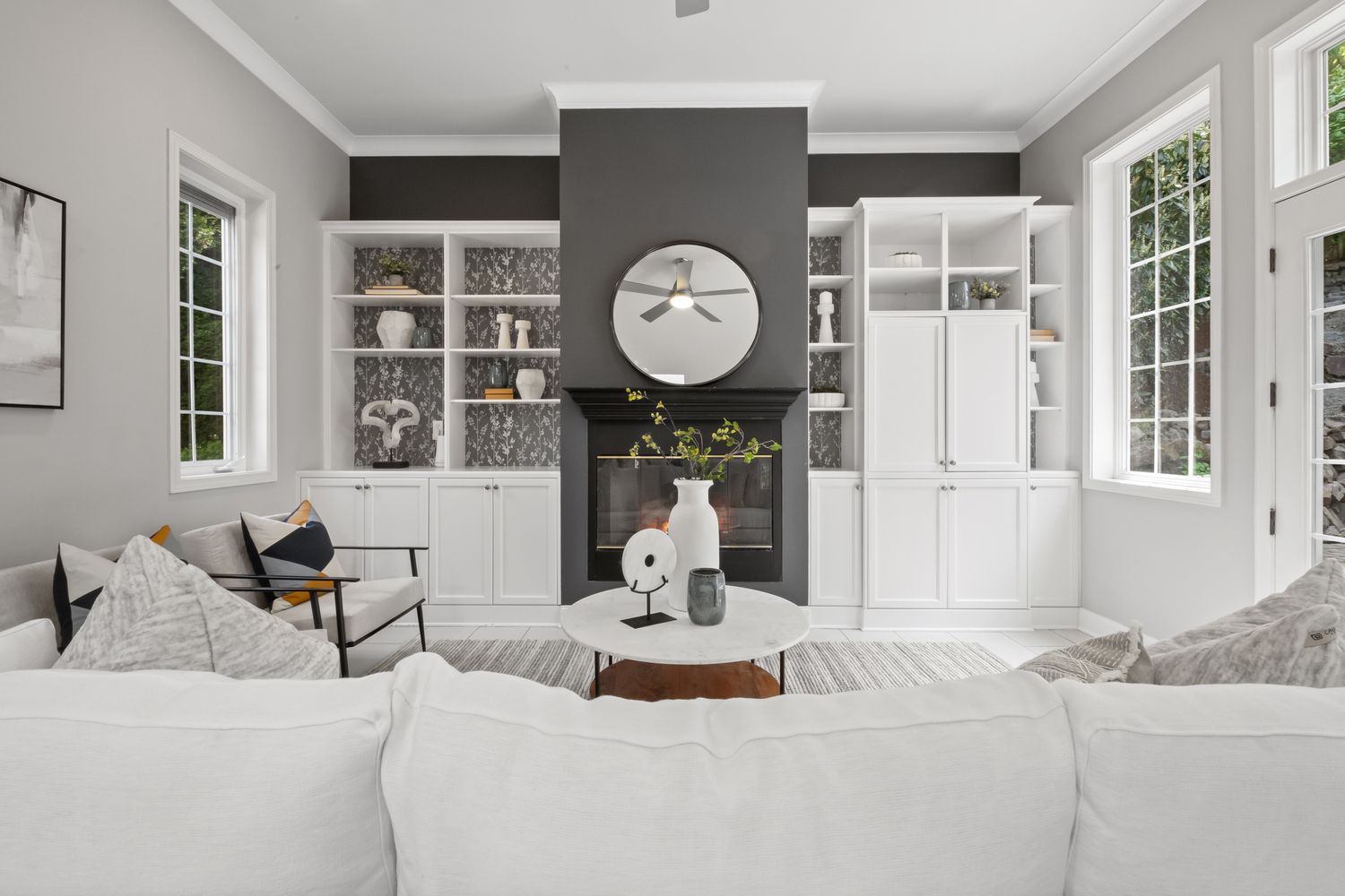 Elegant living room with white sectional sofa, gray fireplace wall, built-in shelving, and abundant natural light.