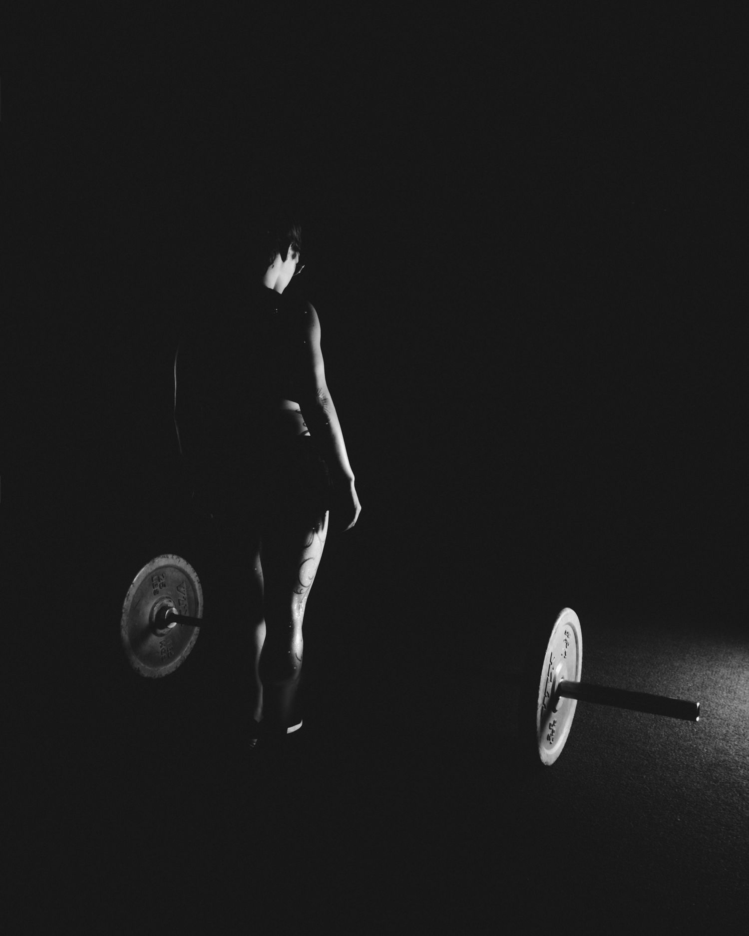Dramatic black and white silhouette of a weightlifter performing a barbell lift in a dimly lit space.