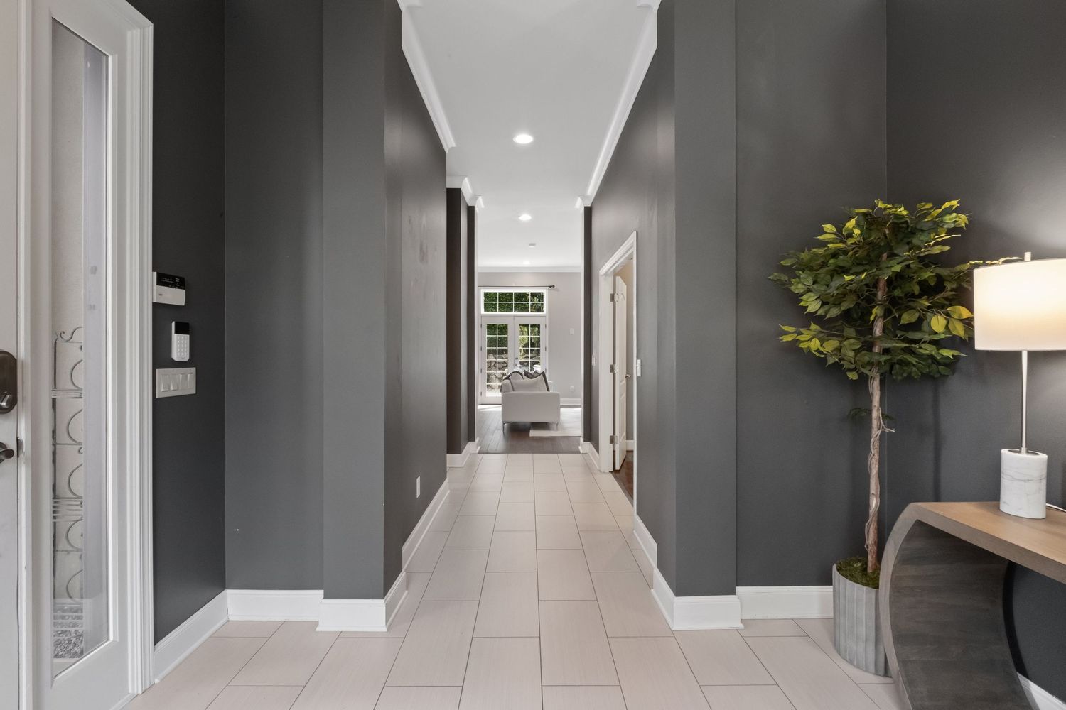 Modern hallway with gray walls, white tile floors and a decorative indoor tree features elegant recessed lighting.