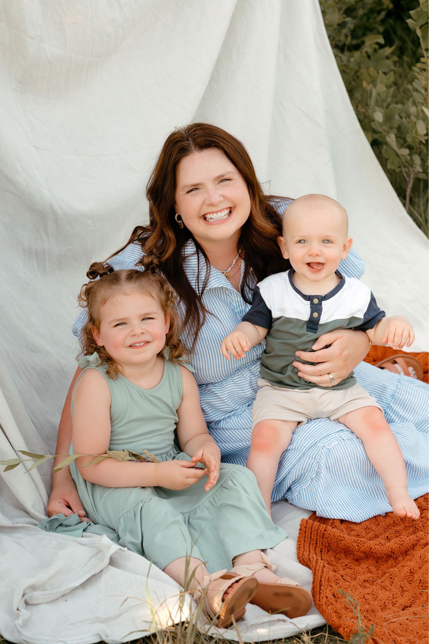 Mom sitting on a blanket outdoors holding her two kids during a family photo session in Brookings, SD.