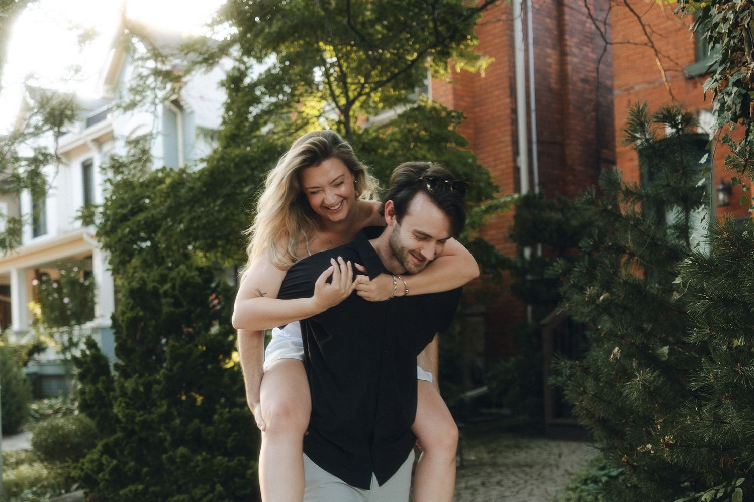 A person giving a piggyback ride outdoors near a house with lush greenery in the background.