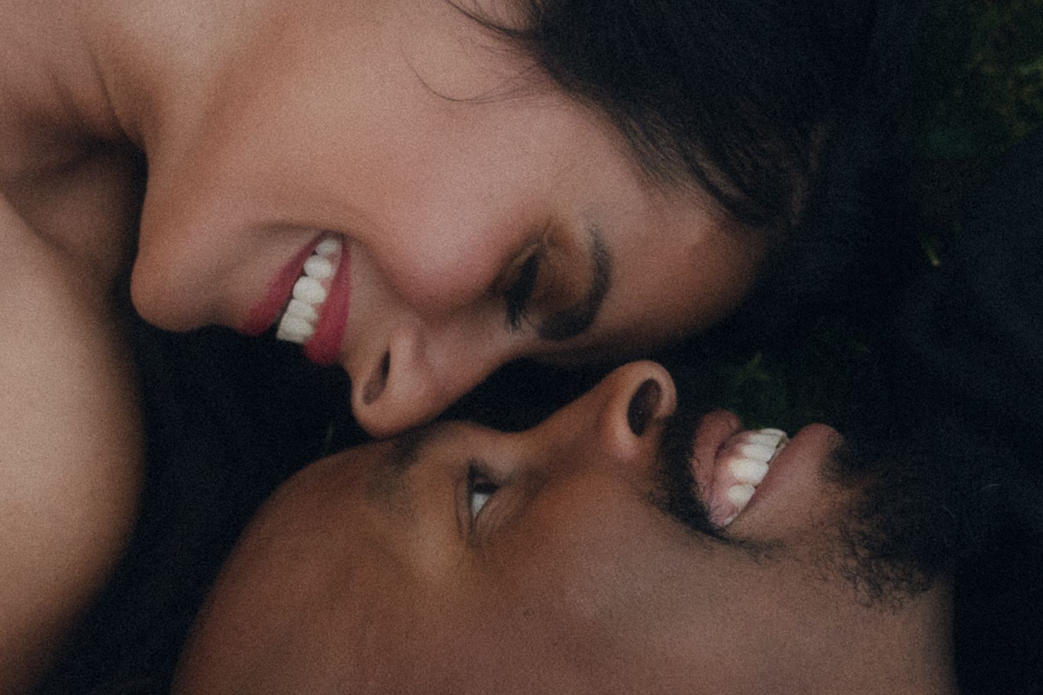 Close-up photo showing warm intimate moment between two people with bright smiles sharing affectionate touch.