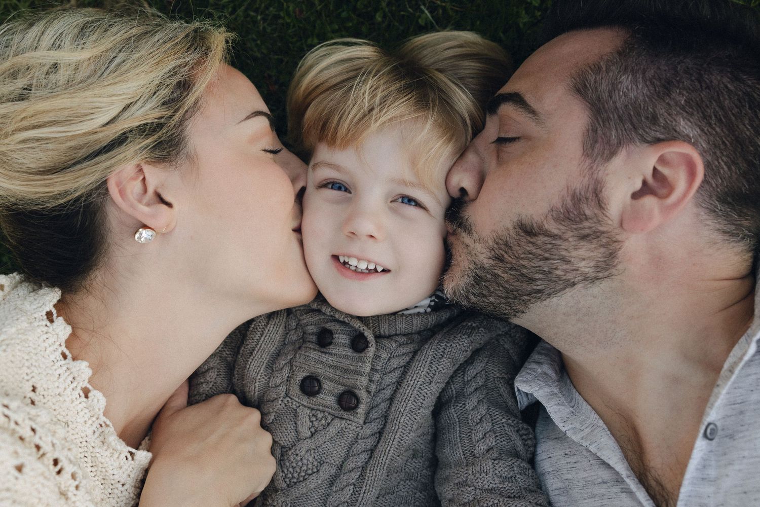 Family of three share sweet close-up kisses and laughter while cuddling together.