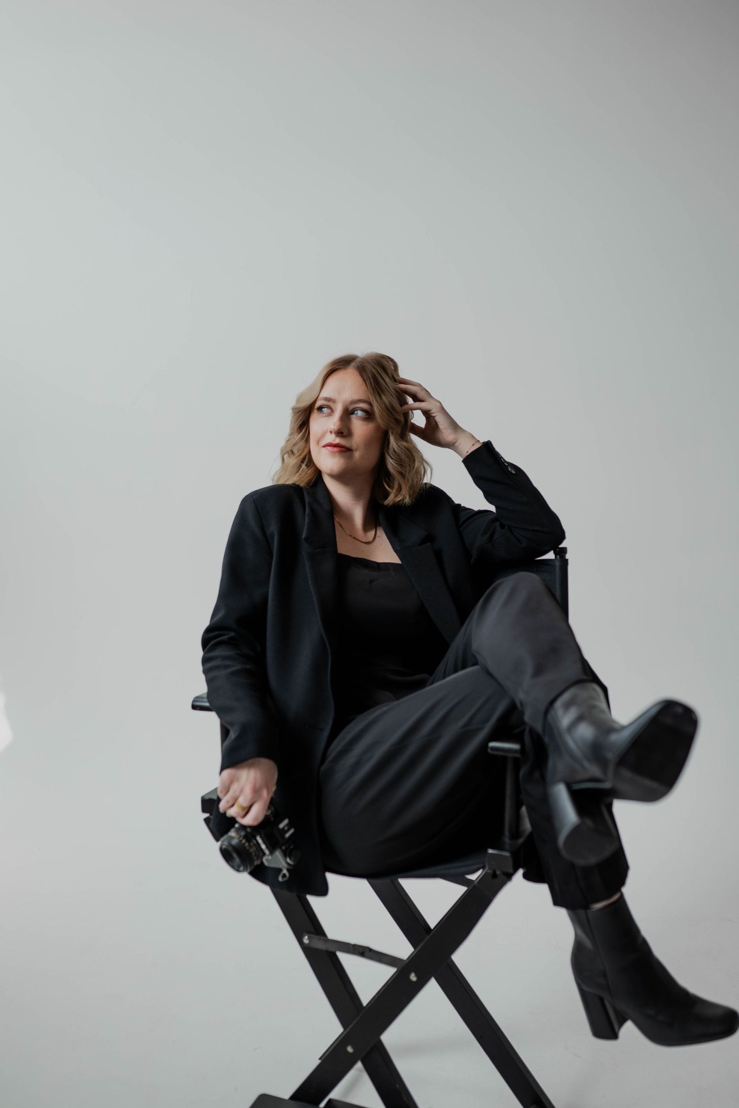Stylish figure in black blazer reclines in director's chair with boots crossed.