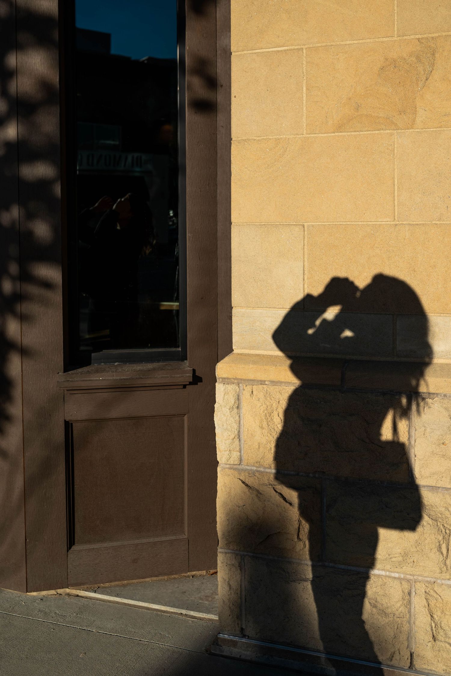 Dramatic shadow of figure cast on beige stone wall beside doorway in late afternoon light.
