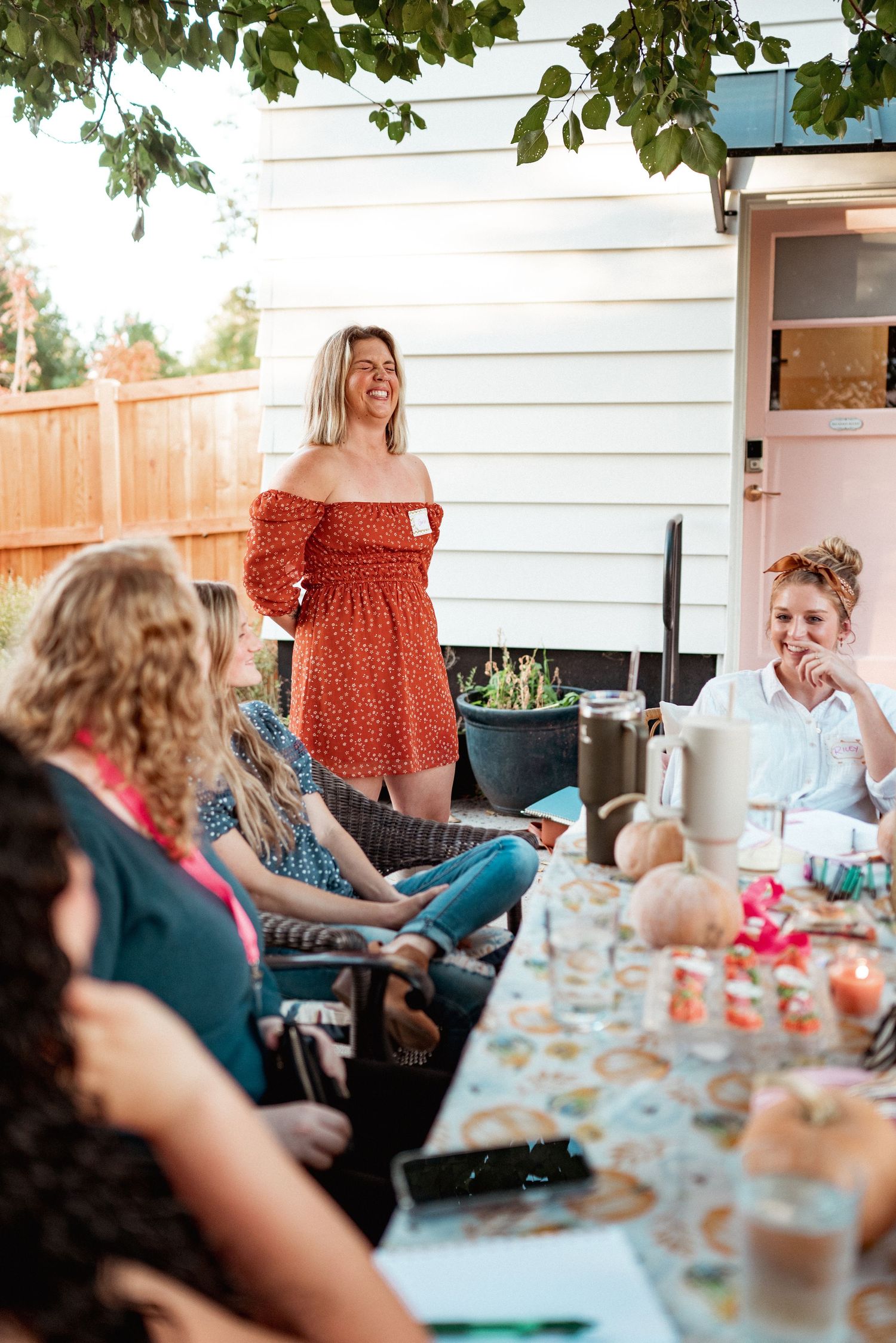 Outdoor gathering with people seated around a decorated table in a backyard setting.