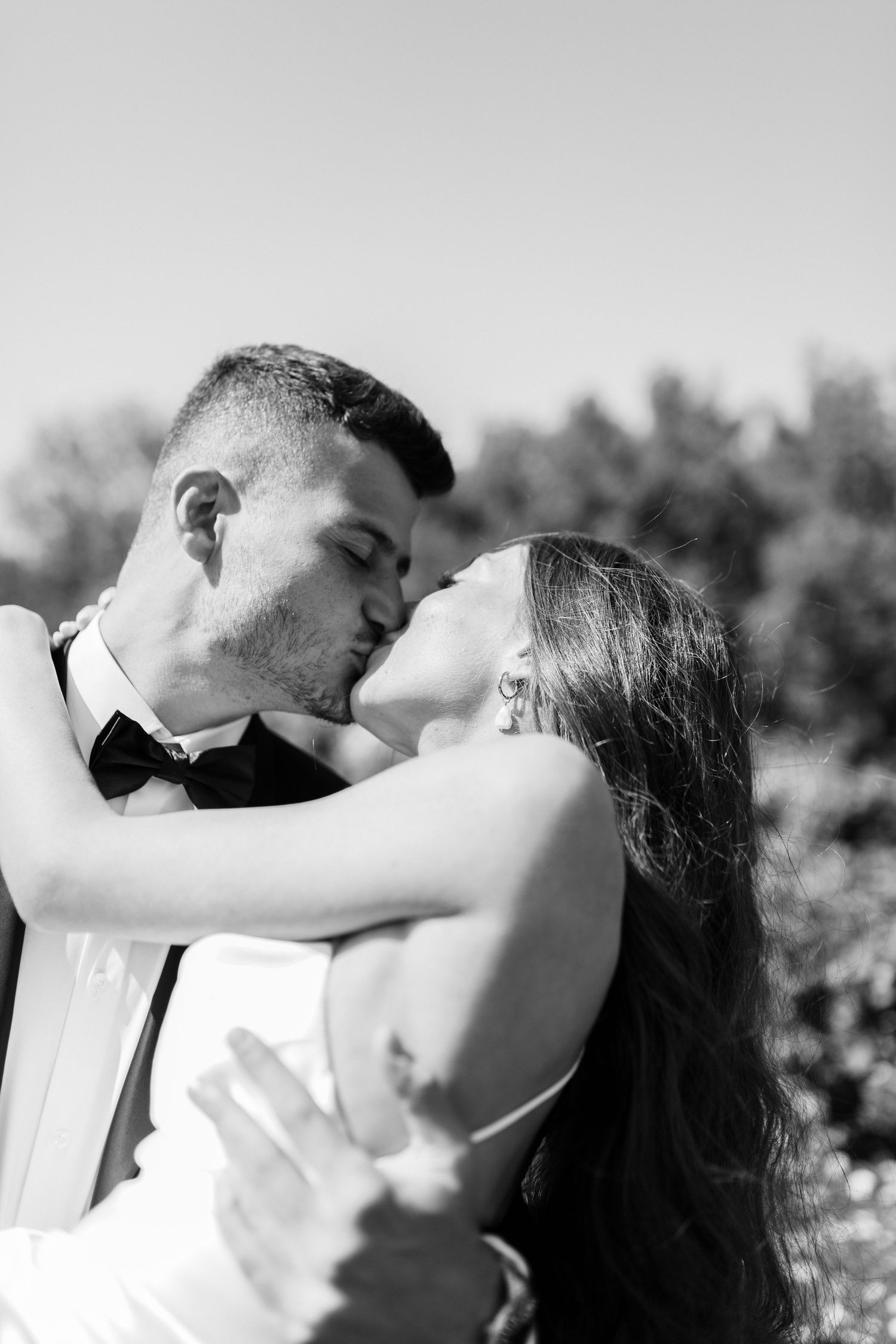 A romantic black and white wedding portrait of a couple sharing a passionate kiss outdoors on their special day.