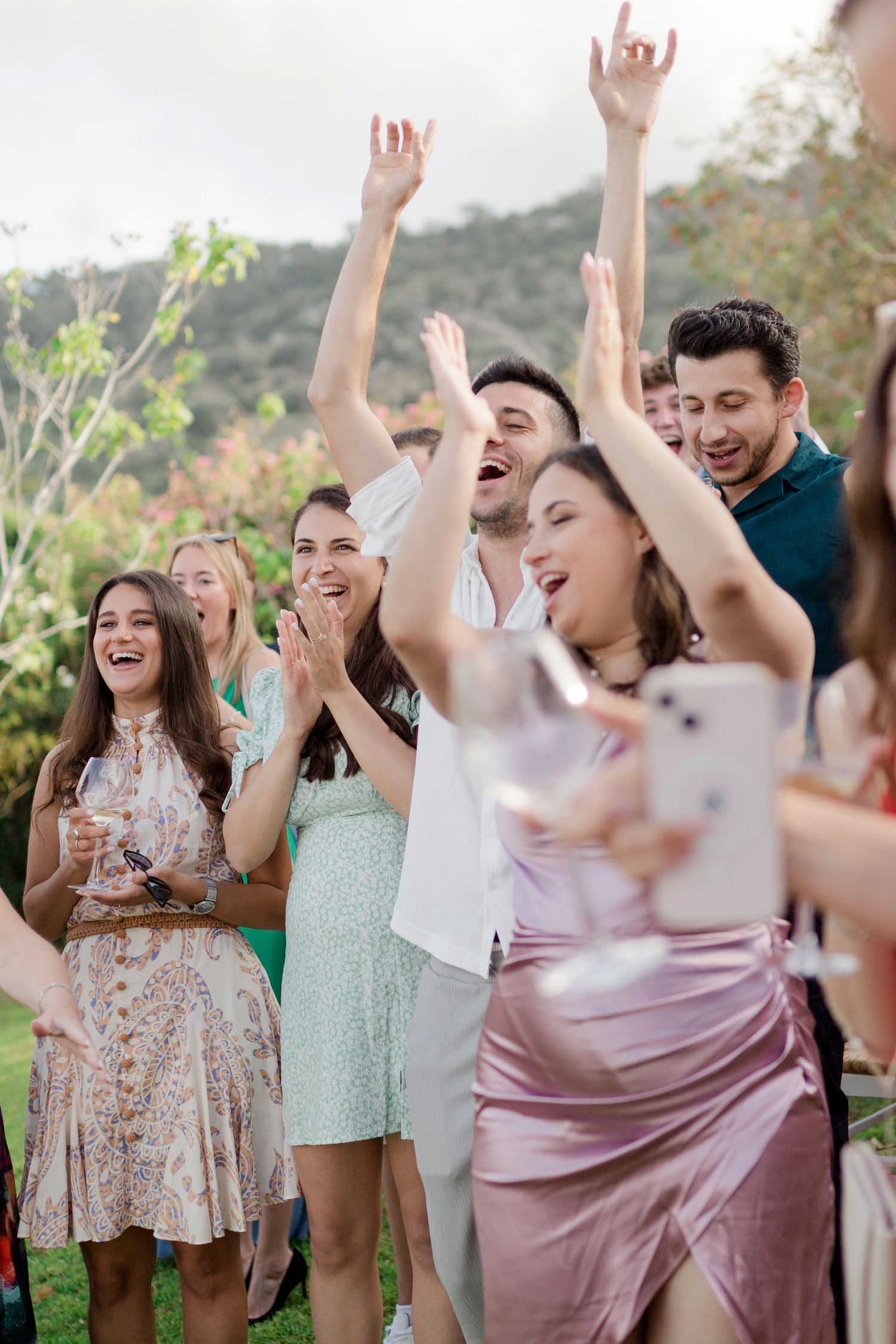 A group of happy party guests celebrating outdoors with raised arms and joyful expressions.