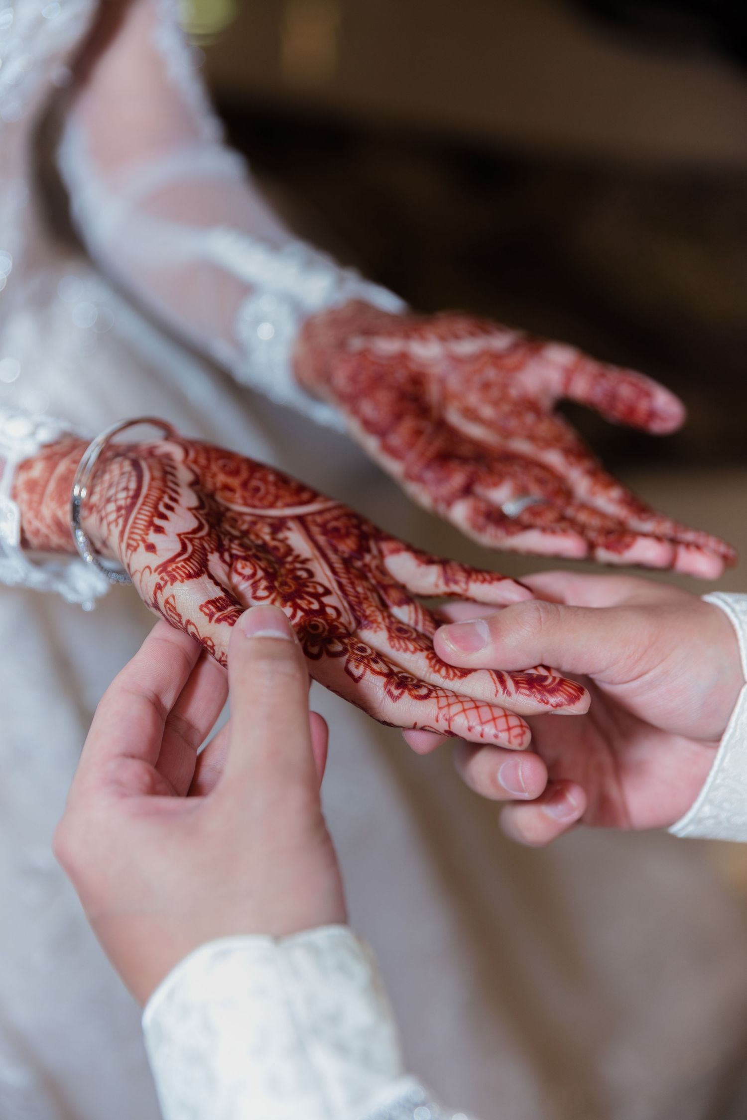 Groom placing a ring on bride's henna-adorned hand during a traditional South Asian wedding ceremony.