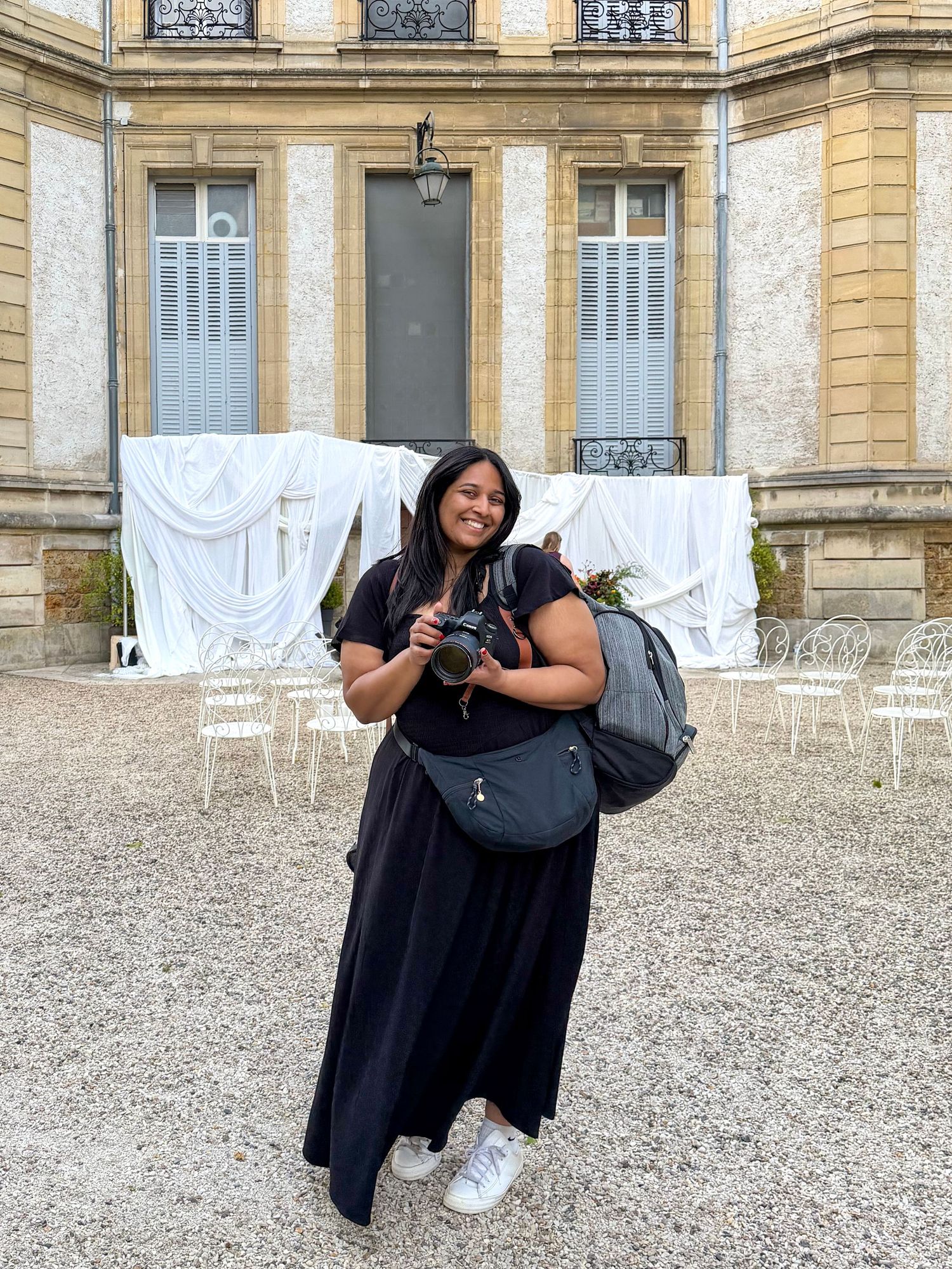 Female Wedding photographer smiling with camera outside a beautiful French chateau destination wedding venue.