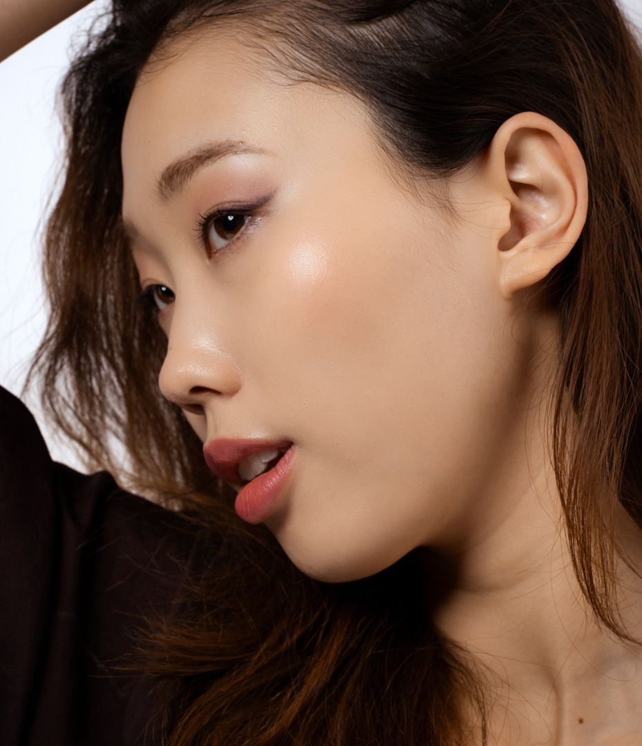 Young Asian woman with glowing skin, subtle eye makeup, and natural lips in a profile pose.