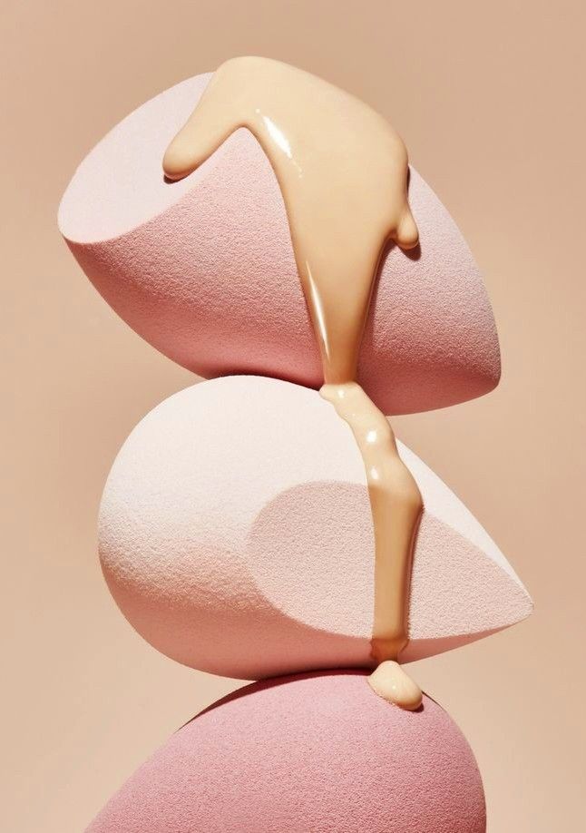 Three pink beauty blender sponges stacked with foundation makeup dripping over them.