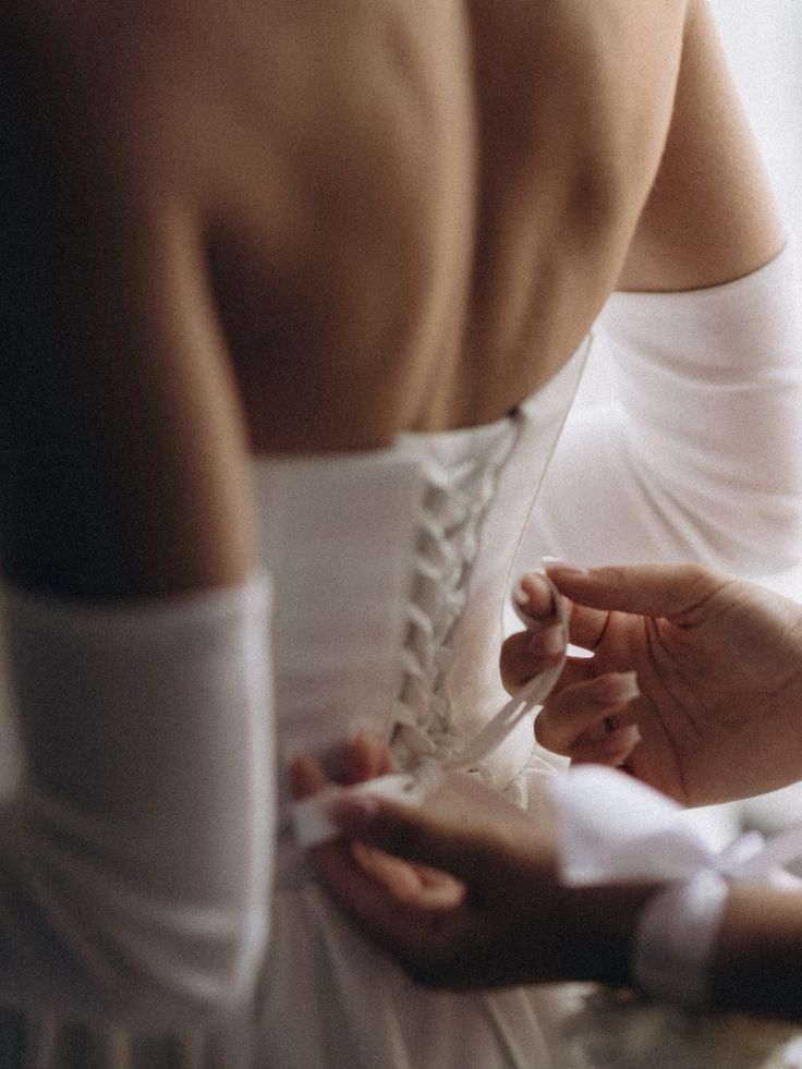 Wedding dress being laced up the back by a helper's hands.