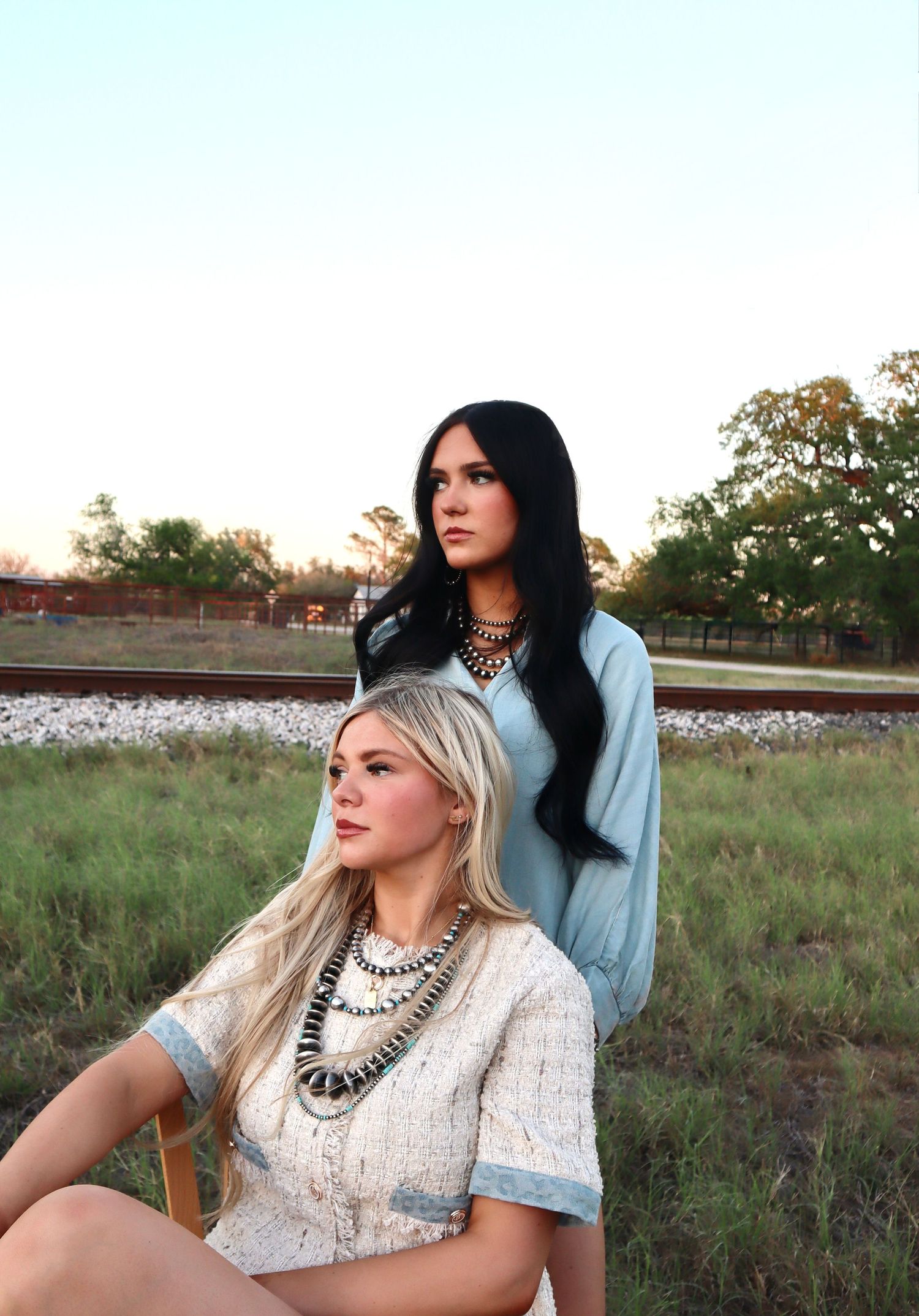 Two people pose in a cotton field at sunset wearing western-inspired fashion and statement necklaces.