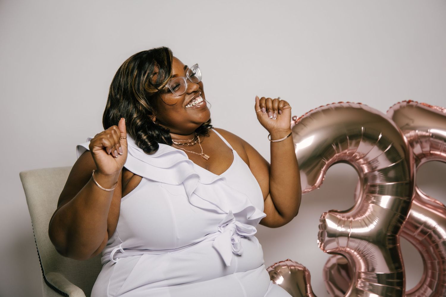 Joyful Black woman celebrating 35th birthday in white dress with rose gold balloons.