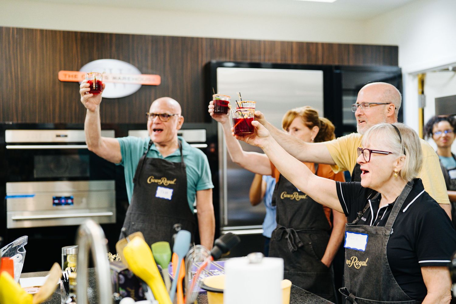 Group of cooking class participants raise their drinks in a toast in a kitchen.