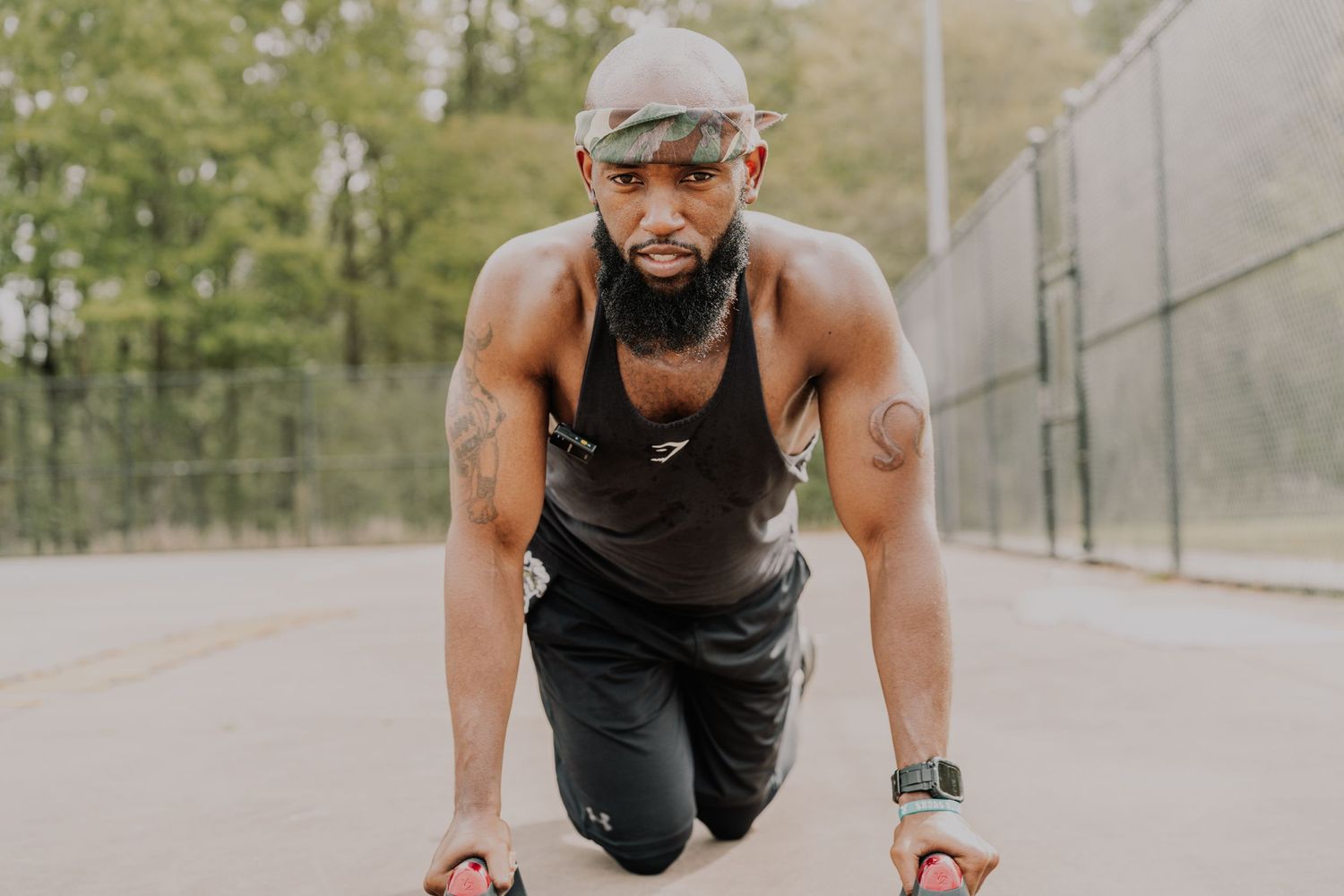 Athletic Black man in starting position on outdoor court wearing tank top and shorts.