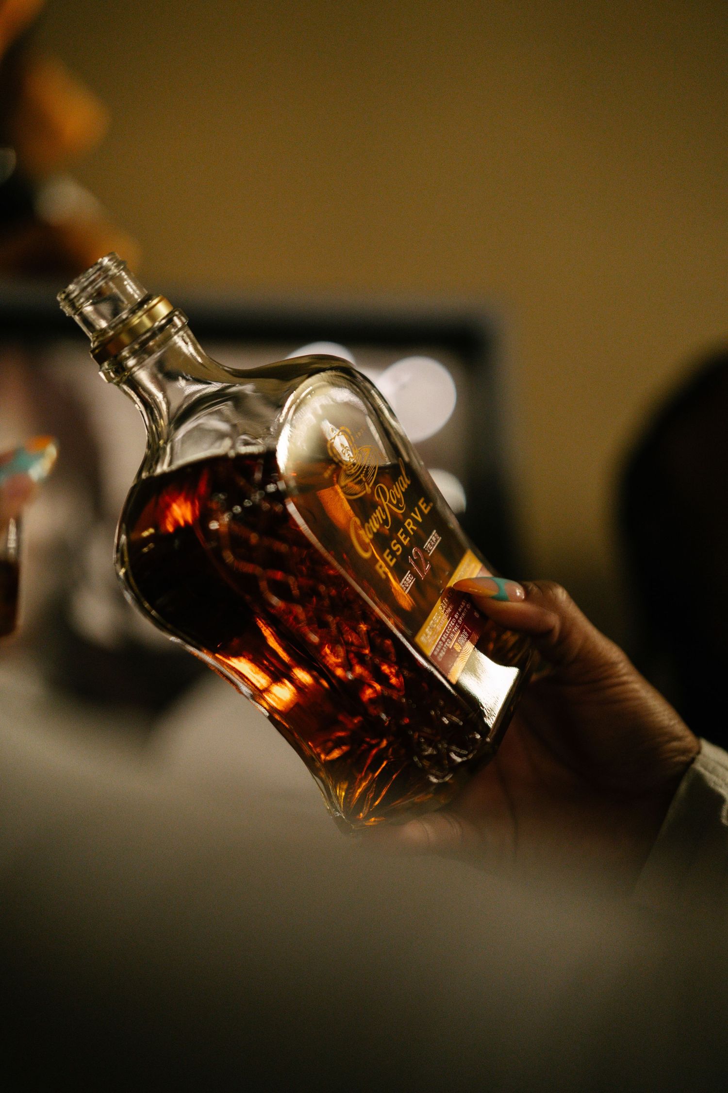 Hand holding a bottle of Reserve whiskey tilted at an angle in dim warm lighting.