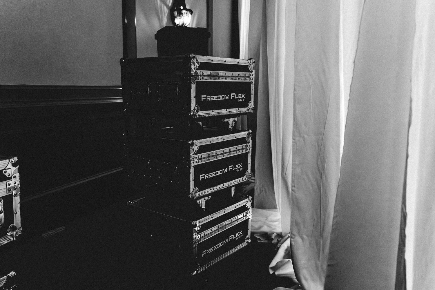 Black and white photo of stacked Freedom Flex flight cases near a window with sheer curtains.