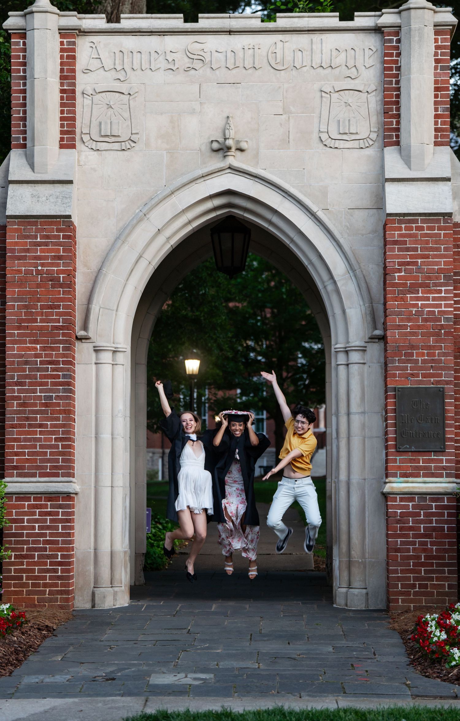 Three students jumping joyfully under the Agnes Scott College brick archway entrance.
