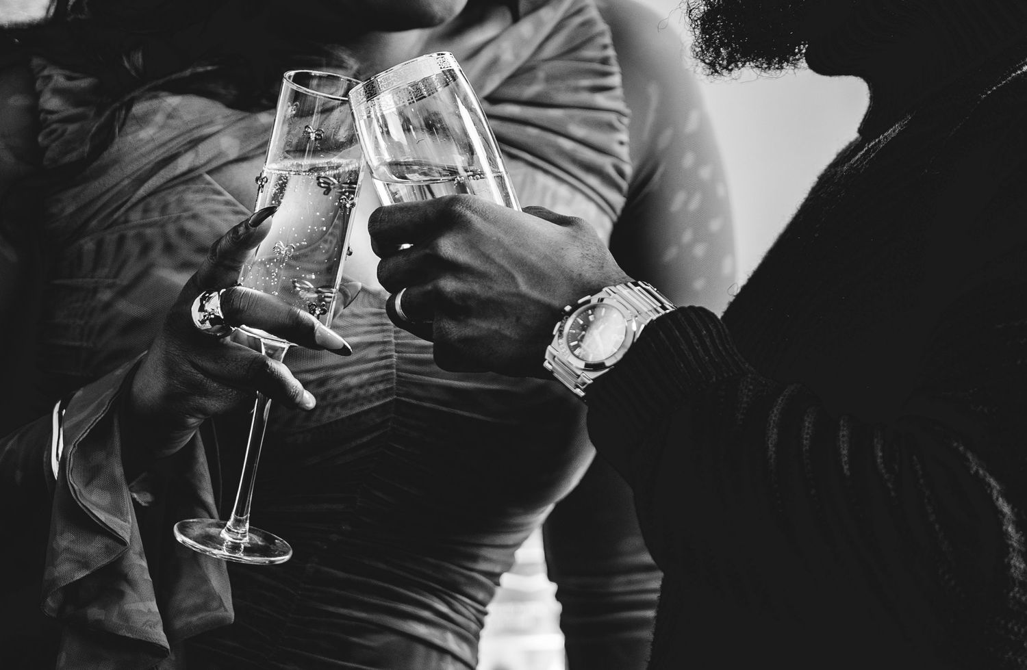 Black and white photo of couple toasting with champagne glasses, man wearing watch.