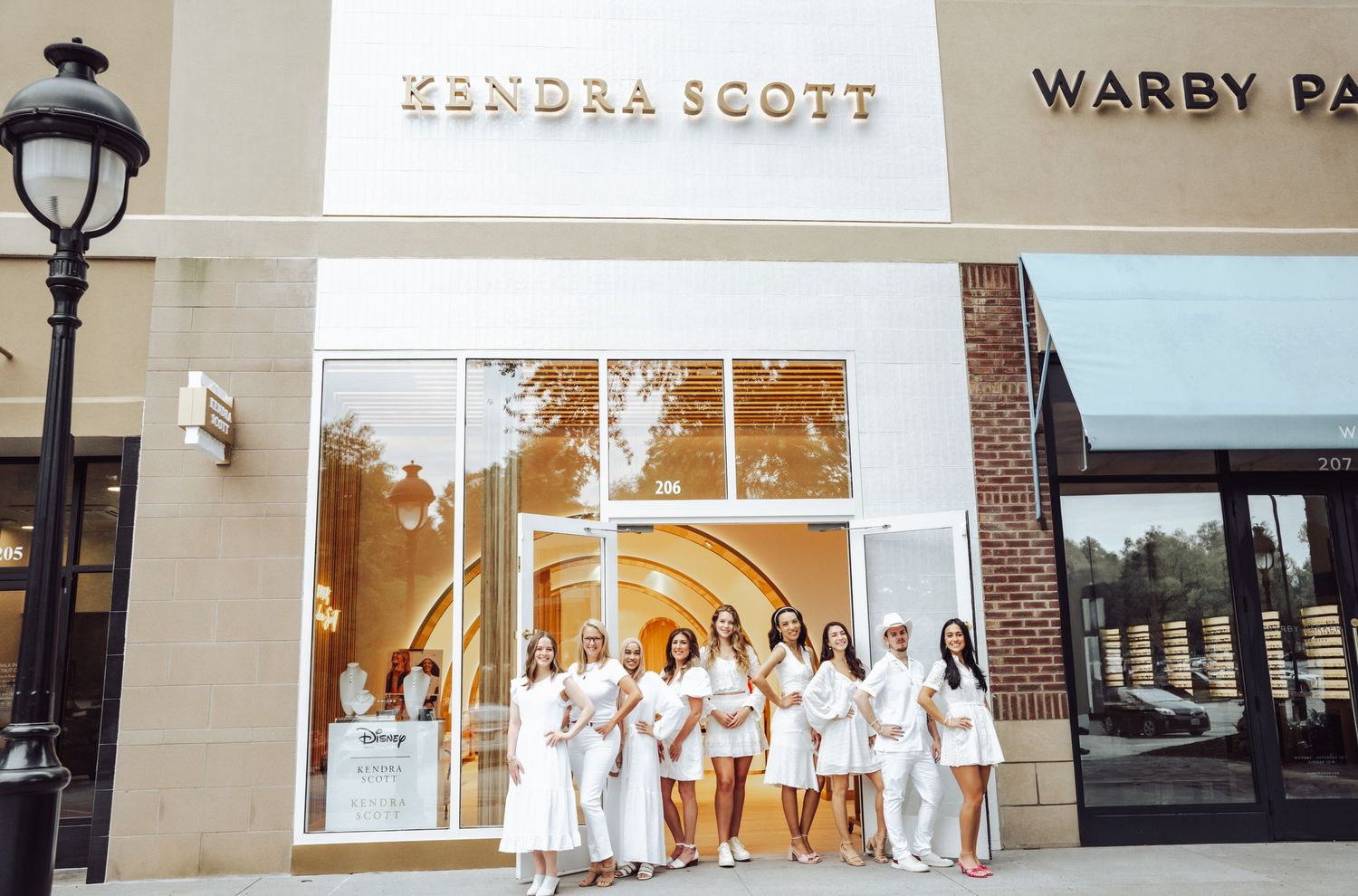 Group of women dressed in white posing outside Kendra Scott and Warby Parker stores.