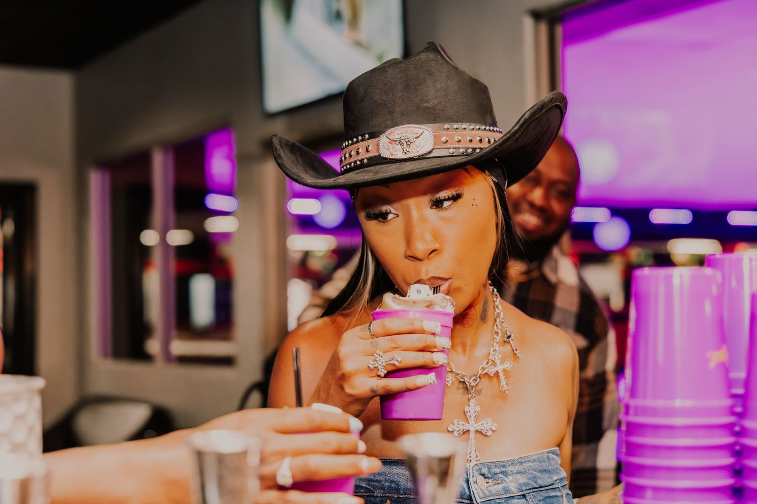 Woman in cowboy hat sips a pink drink at a bar.