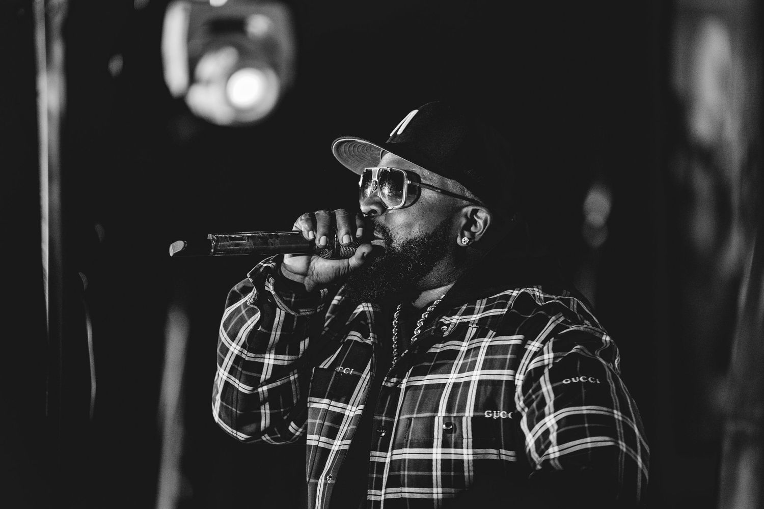 Black and white photo of a male singer performing with a microphone wearing sunglasses and a plaid shirt.