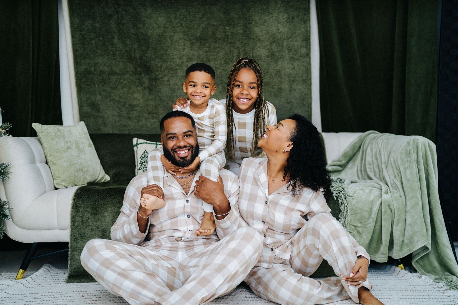 Joyful Black family of four in matching plaid pajamas laughing together on floor.