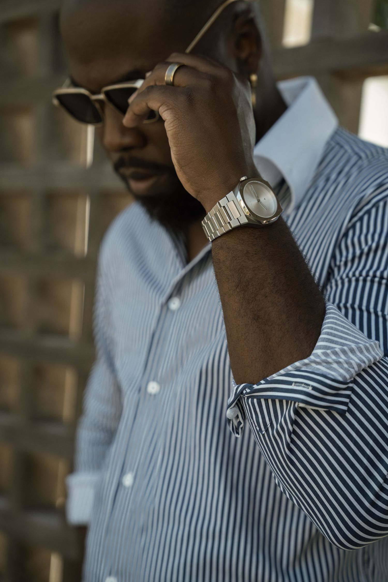 Stylish Black man in striped shirt wearing silver watch and sunglasses, close-up portrait.