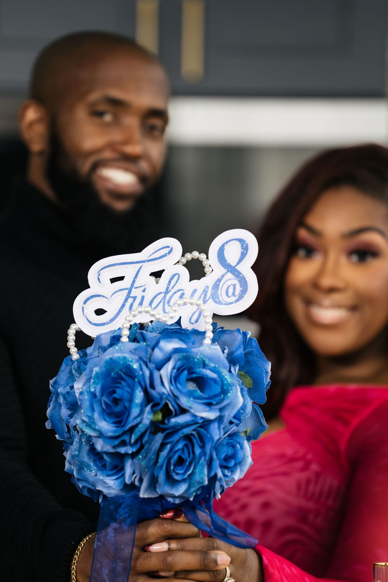 Smiling couple holding blue roses bouquet with Friday@8 sign at a romantic event.