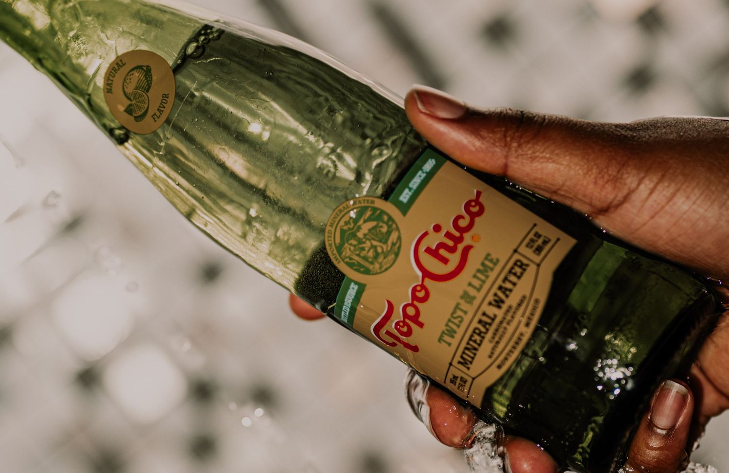 Close-up of a wet Topo Chico Twist of Lime mineral water bottle held in hand.