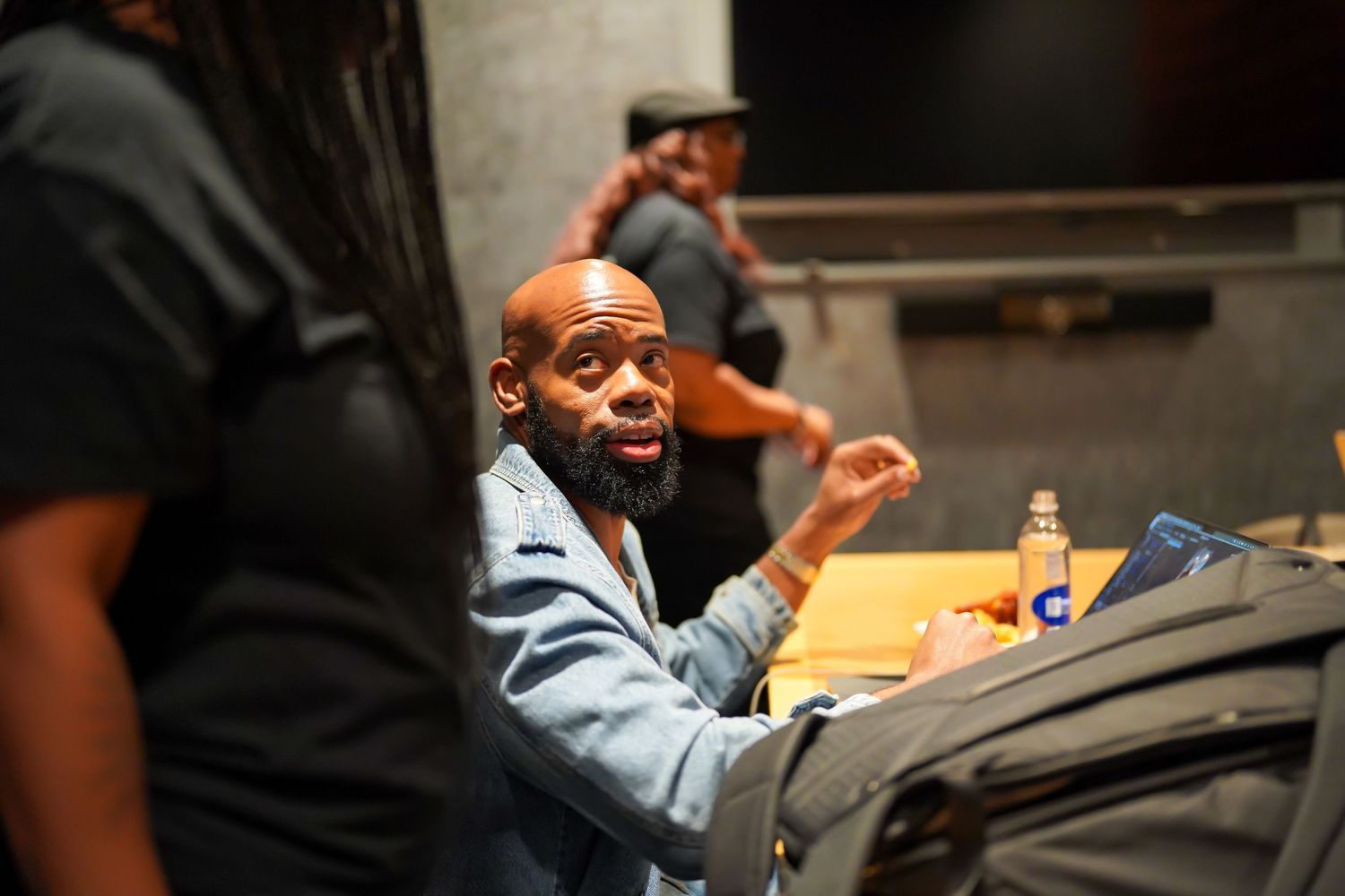Man with beard sitting at table gesturing during a discussion at an indoor event.